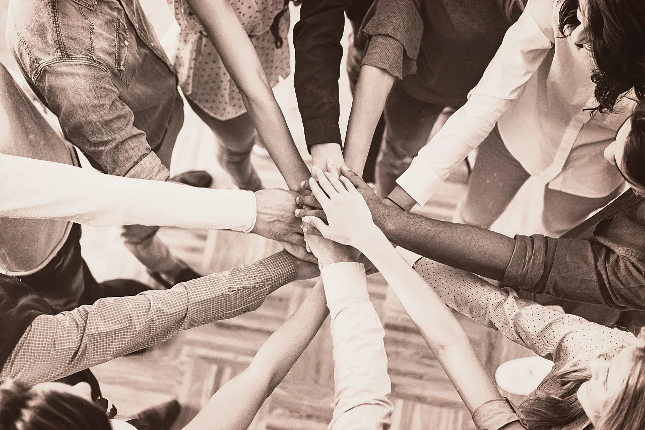 Group of diverse people standing in a circle with hands stacked together in the center.