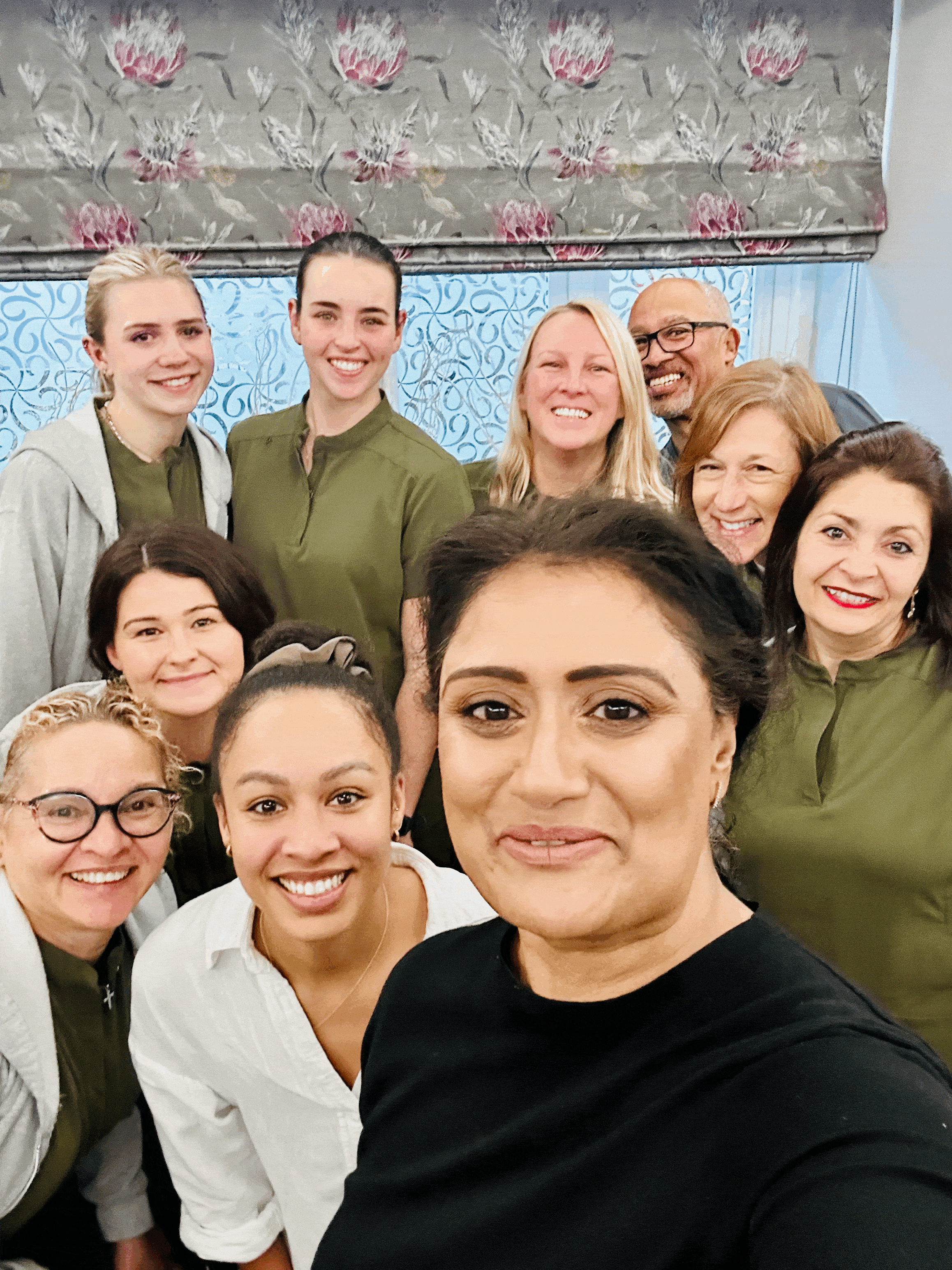Smiling dental team in olive green tunics crowding into a group selfie
