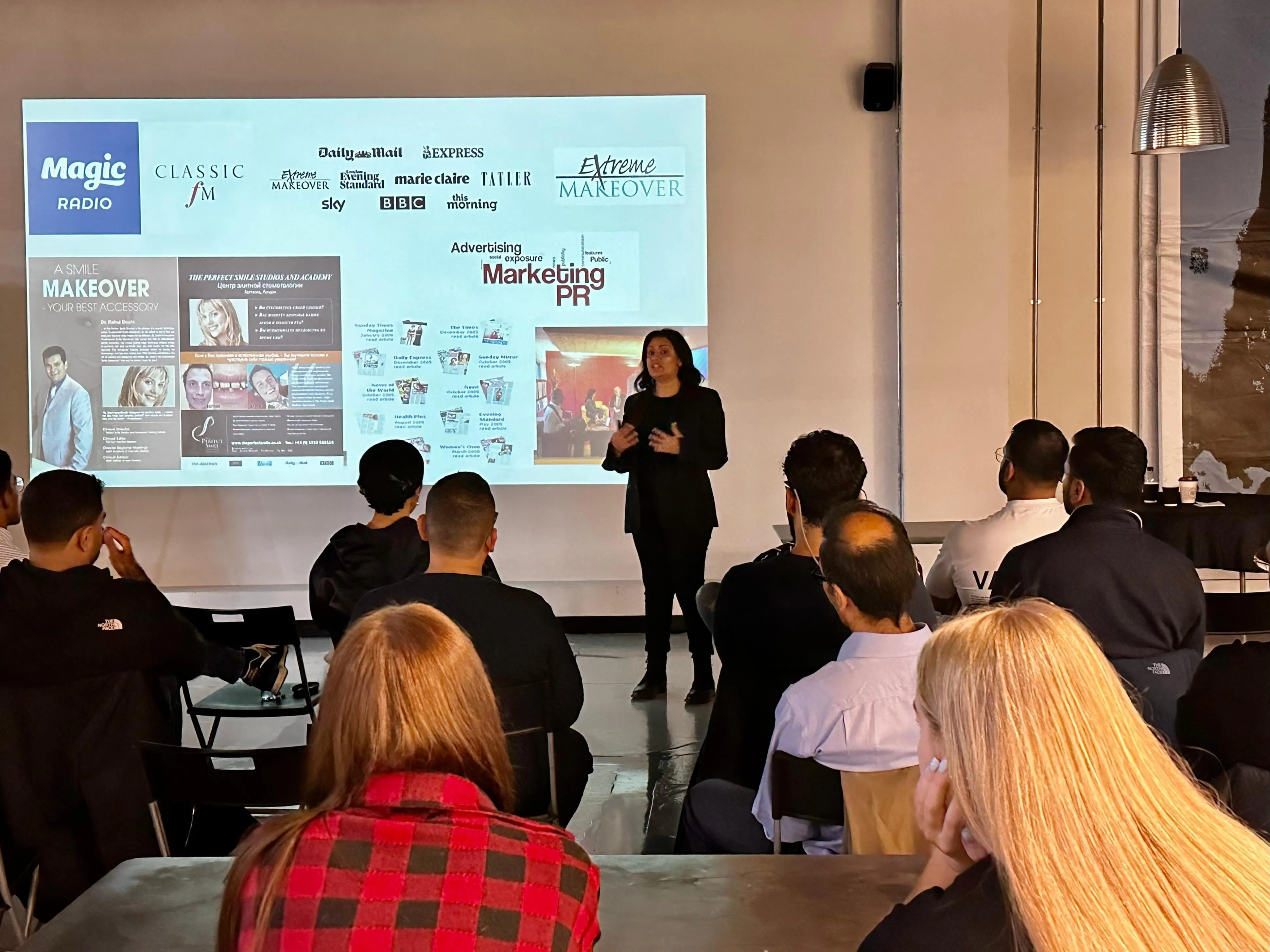 Woman presenting a marketing and PR slide to a seated audience in a workshop room