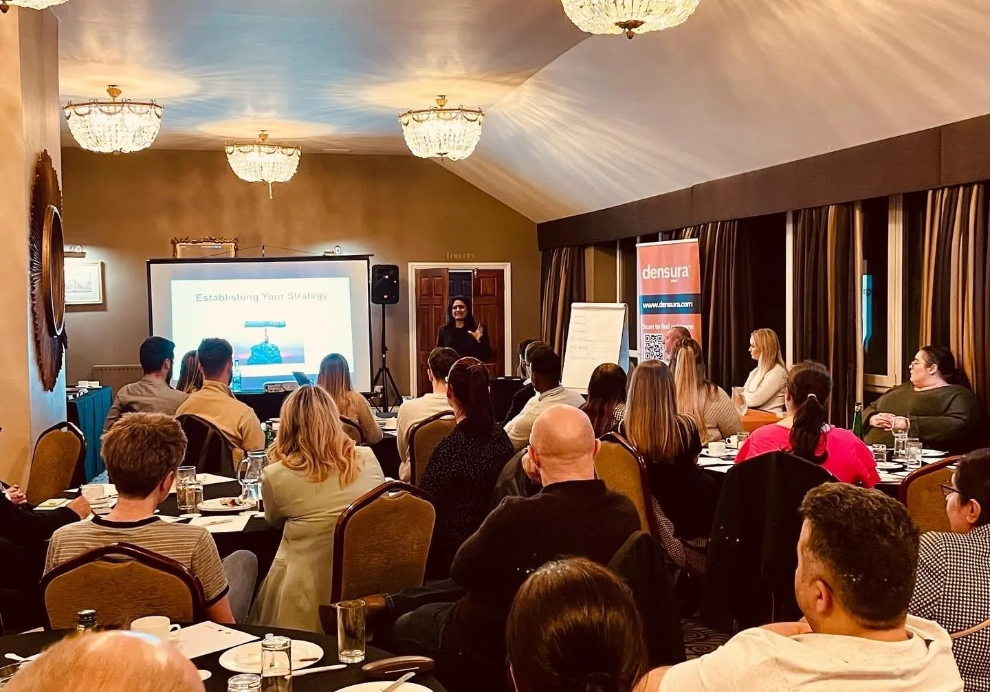 Speaker presenting to dentists seated at tables in a chandeliered function room