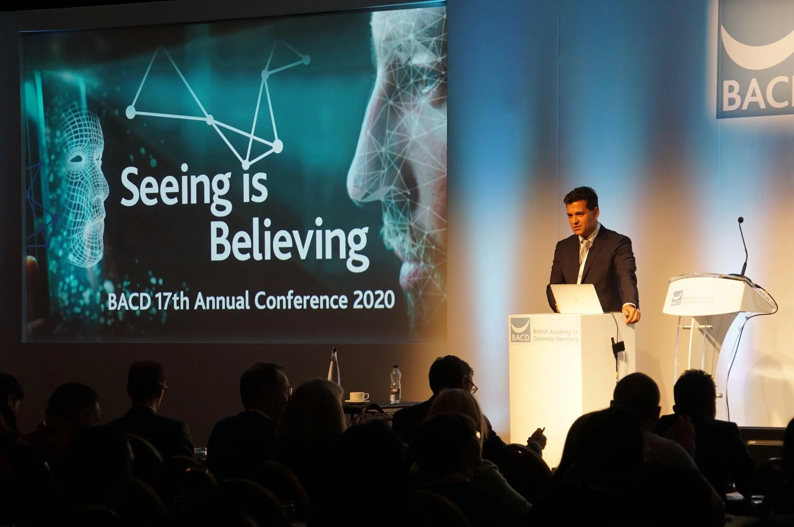 Speaker at a podium beside a 'Seeing is Believing' slide at the BACD 17th Annual Conference 2020