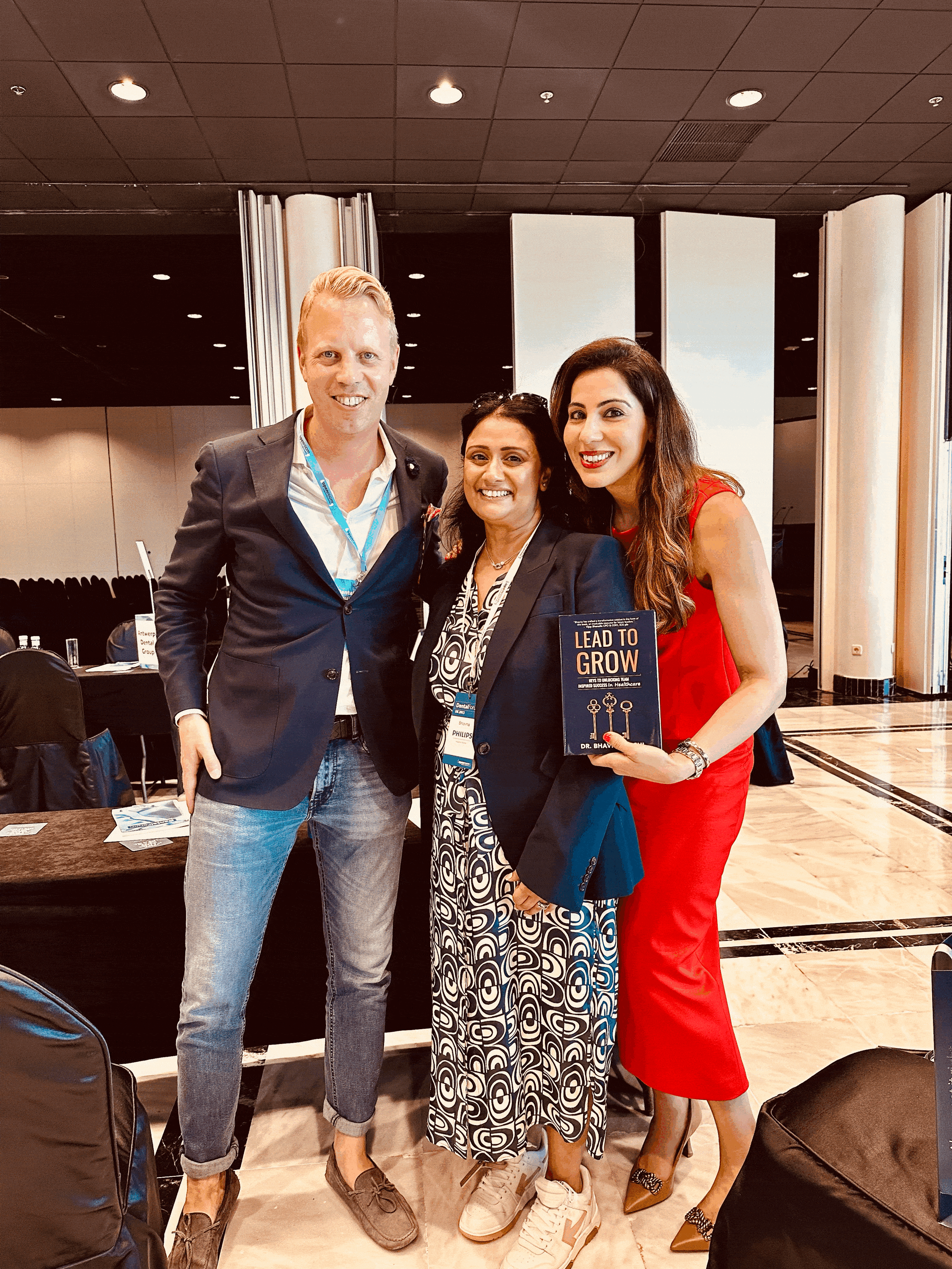 Three smiling people posing at a dental conference, one holding the book 'Lead to Grow'