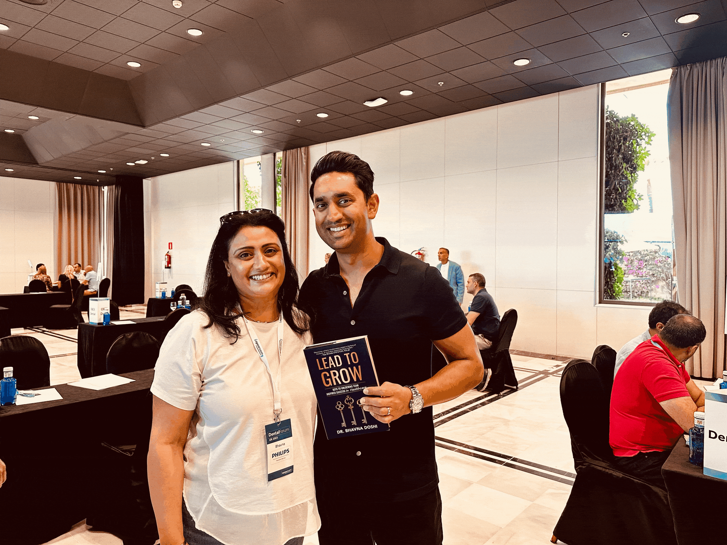 Two smiling people at a Dental Forum event, one holding the book 'Lead to Grow'