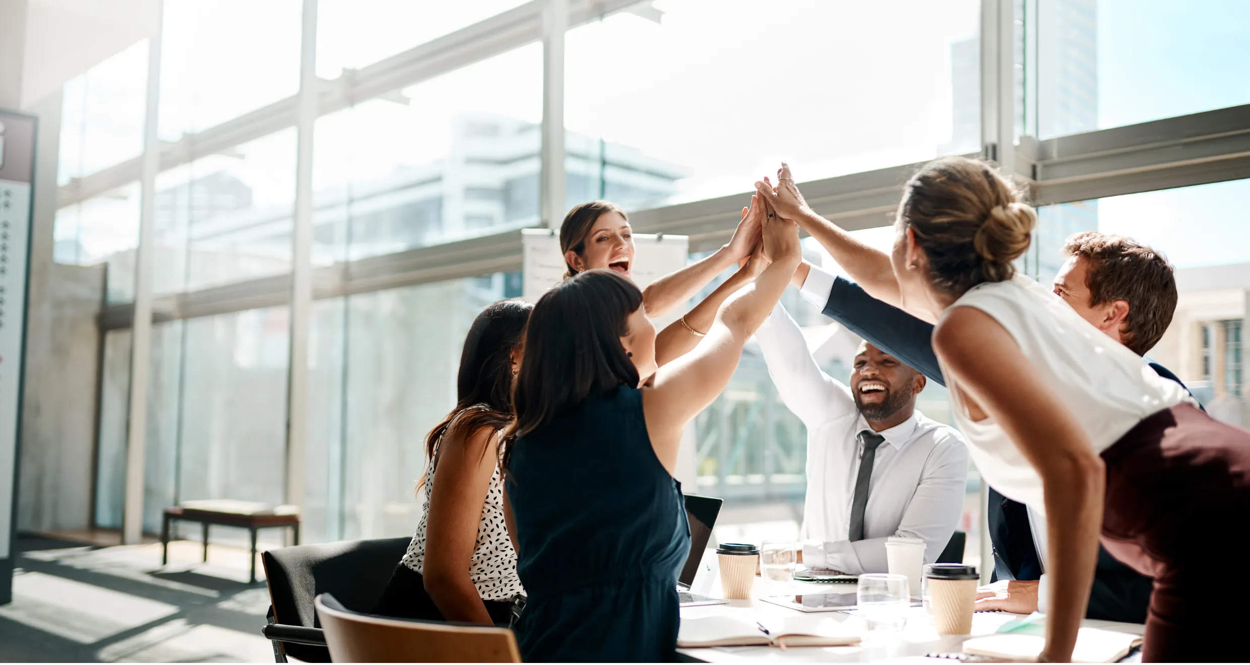 Team members giving a group high five around a table in a bright office