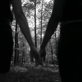 Hands touching in the foreground, with a forest in the background.