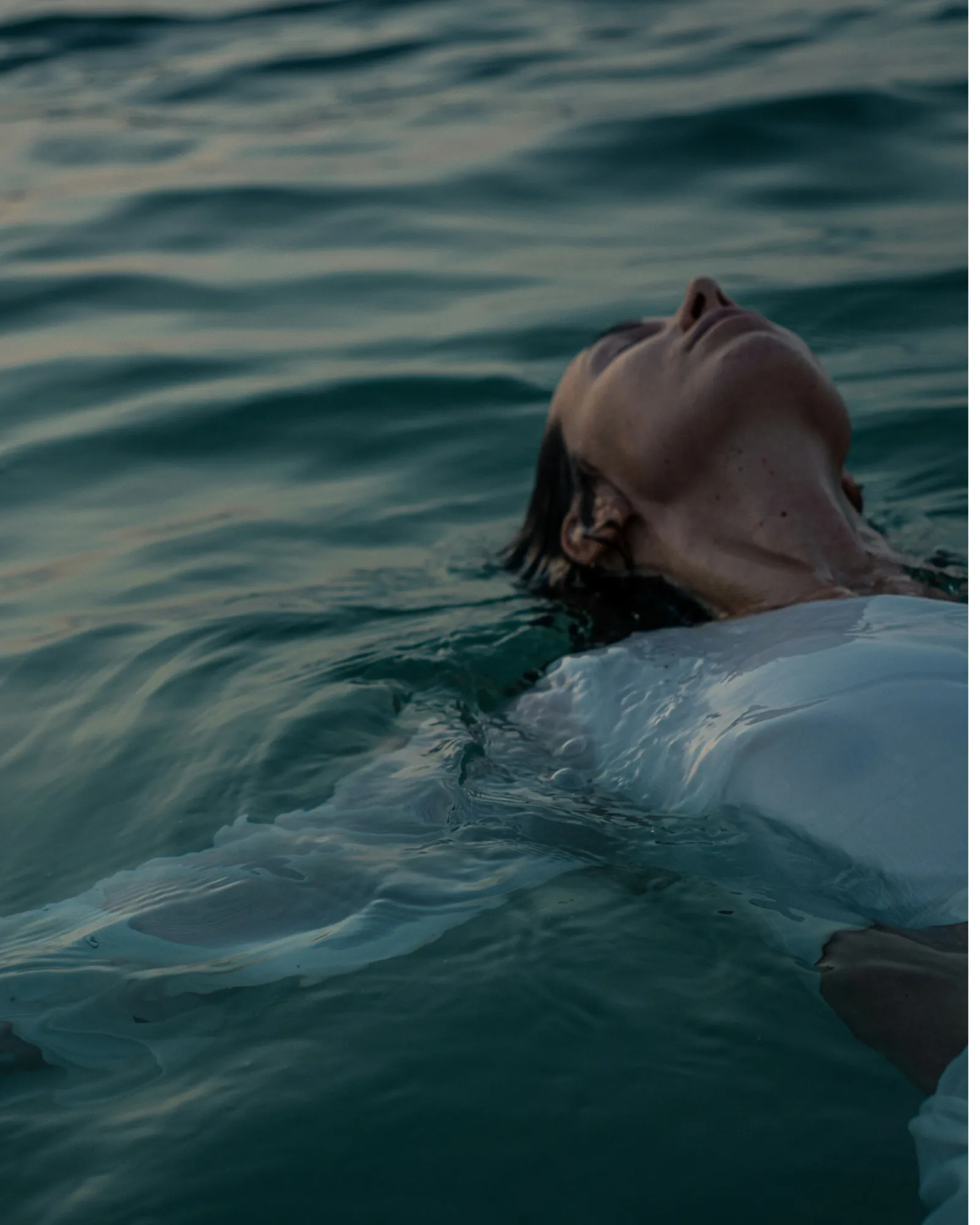 Woman floating peacefully on her back in calm water with eyes closed.