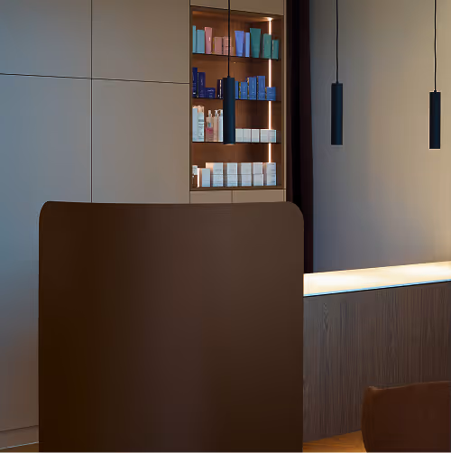 Modern interior with brown partition, illuminated shelves holding cosmetic products, and two black hanging pendant lights.
