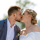 Couple kissing outdoors with clear blue sky background, dressed in formal attire.