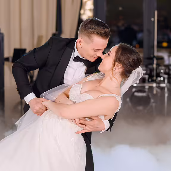 Groom in black tuxedo gently dipping bride in white wedding gown as they gaze into each other's eyes.