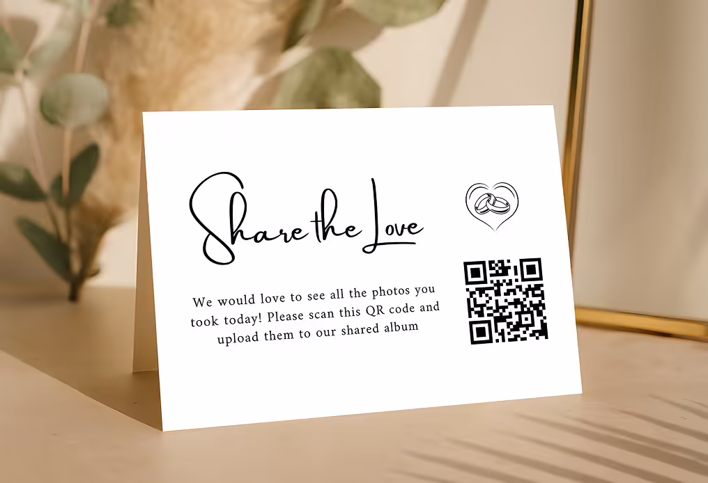 Table card reading 'Share the Love' with a heart and wedding rings illustration and a QR code inviting guests to upload photos to a shared album.