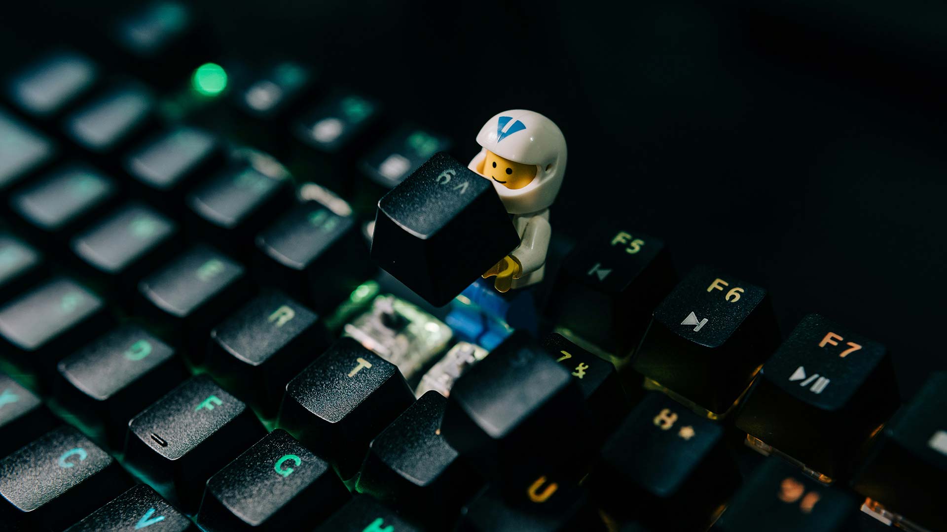 LEGO figure with a helmet holding a removed keycap on a mechanical keyboard with several removed keycaps around.