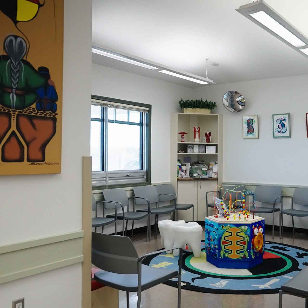 Children's waiting area with gray chairs, colorful play cube, large tooth-shaped seat, and wall art.