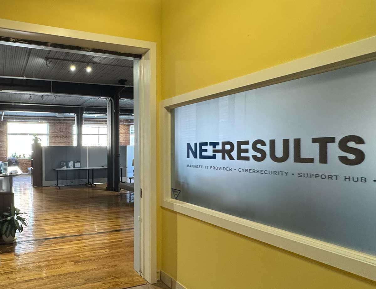 Office entrance with glass panel displaying NET+RESULTS and services like managed IT provider and cybersecurity.