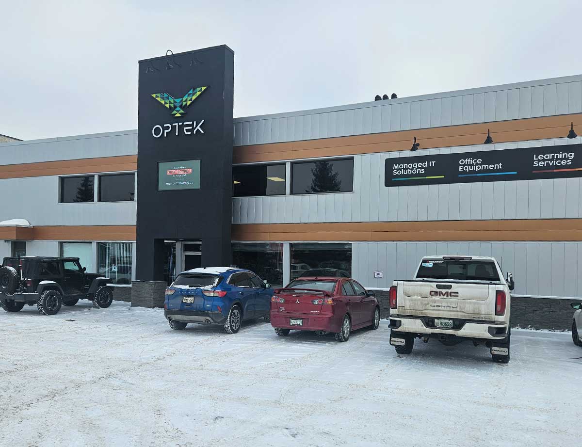 Office building with 'OPTEK' sign and parked cars in a snowy lot, featuring signs for Managed IT Solutions, Office Equipment, and Learning Services.