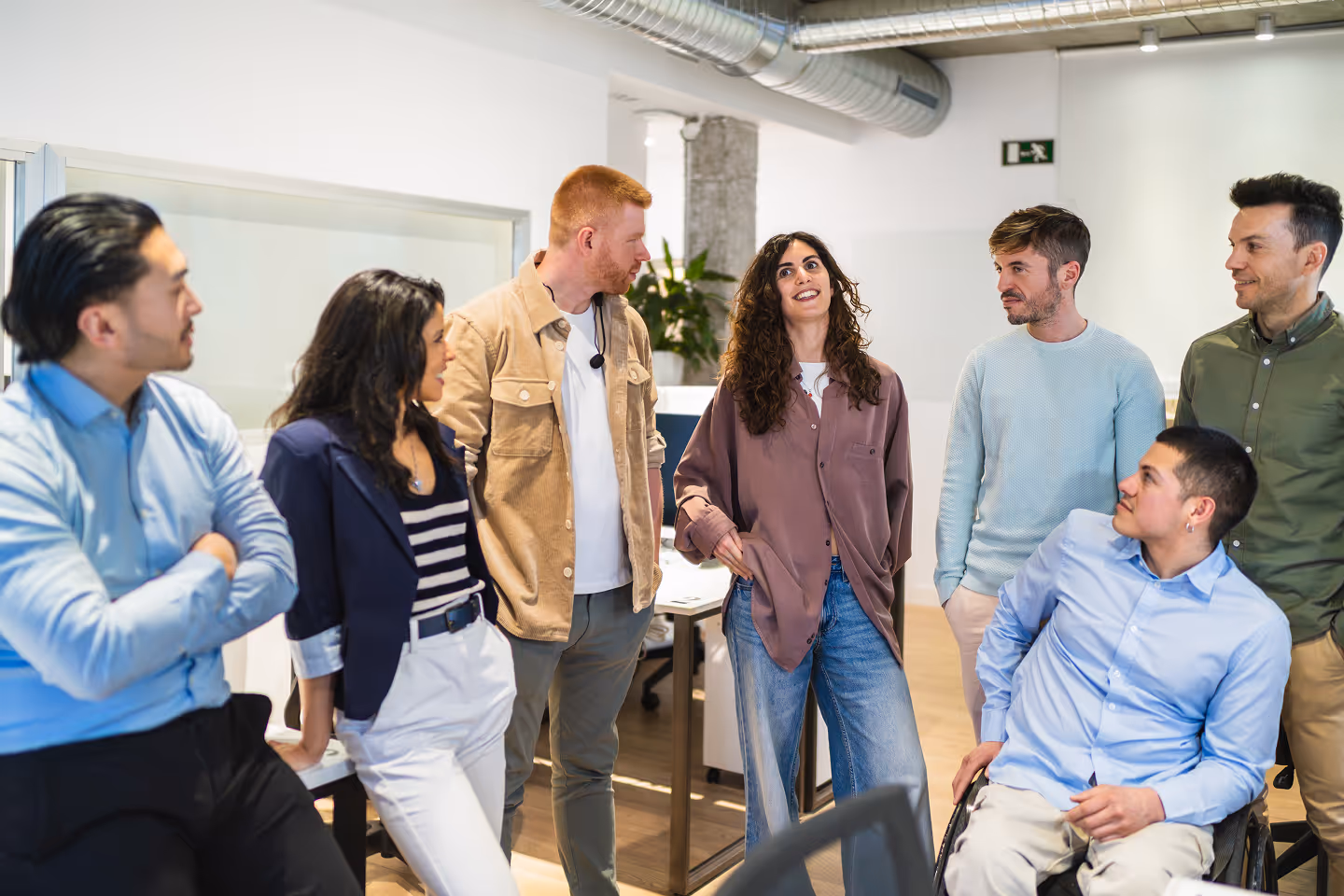 Diverse group of six coworkers having a discussion in a modern office, with one person in a wheelchair.
