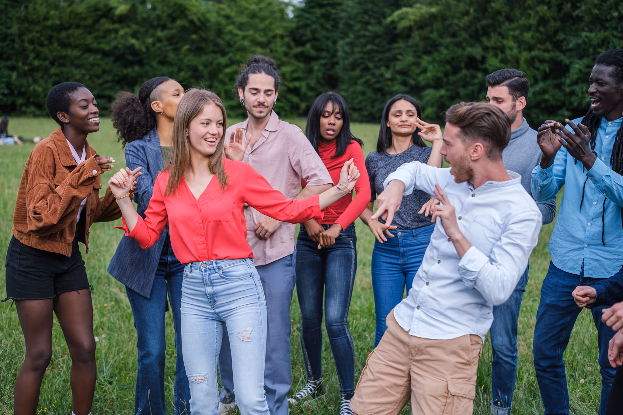 A diverse group of young adults dancing and enjoying themselves outdoors in a grassy area.
