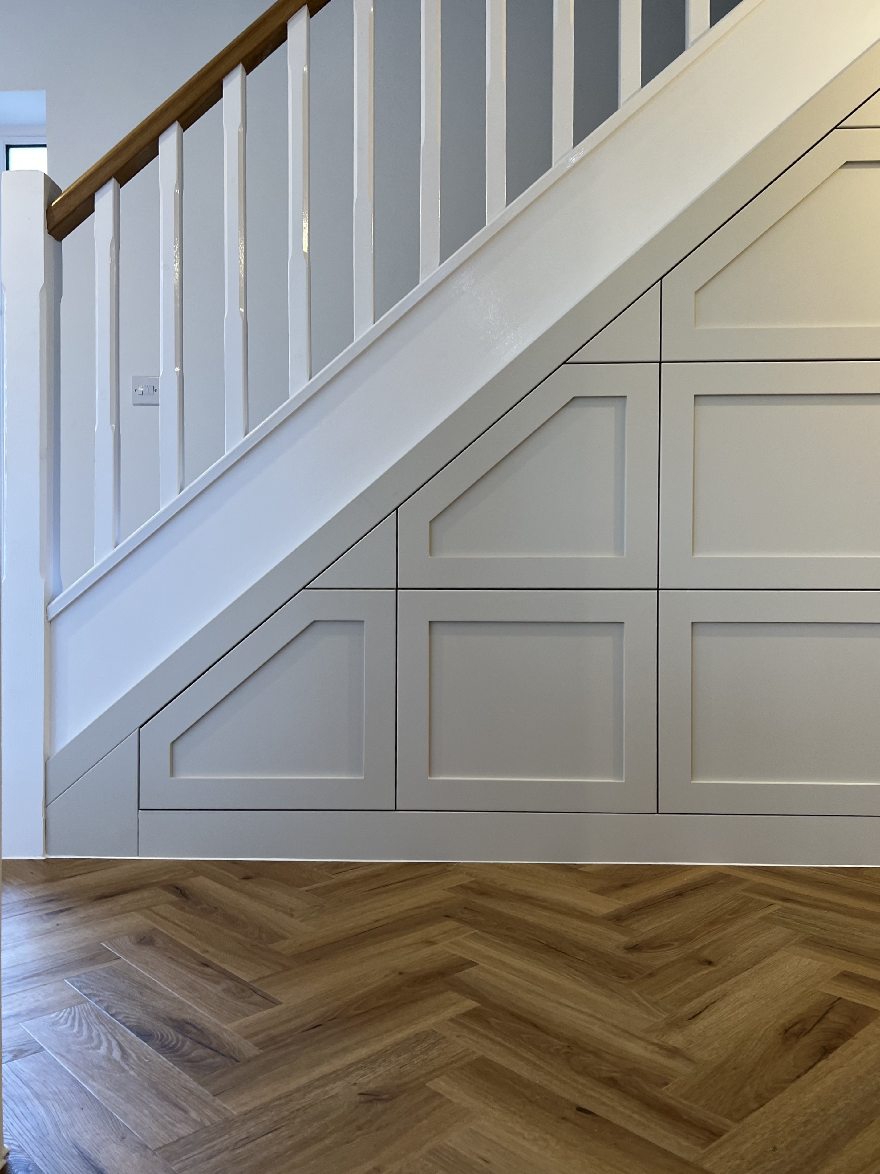 White staircase with built-in storage cabinets underneath and herringbone wood flooring.