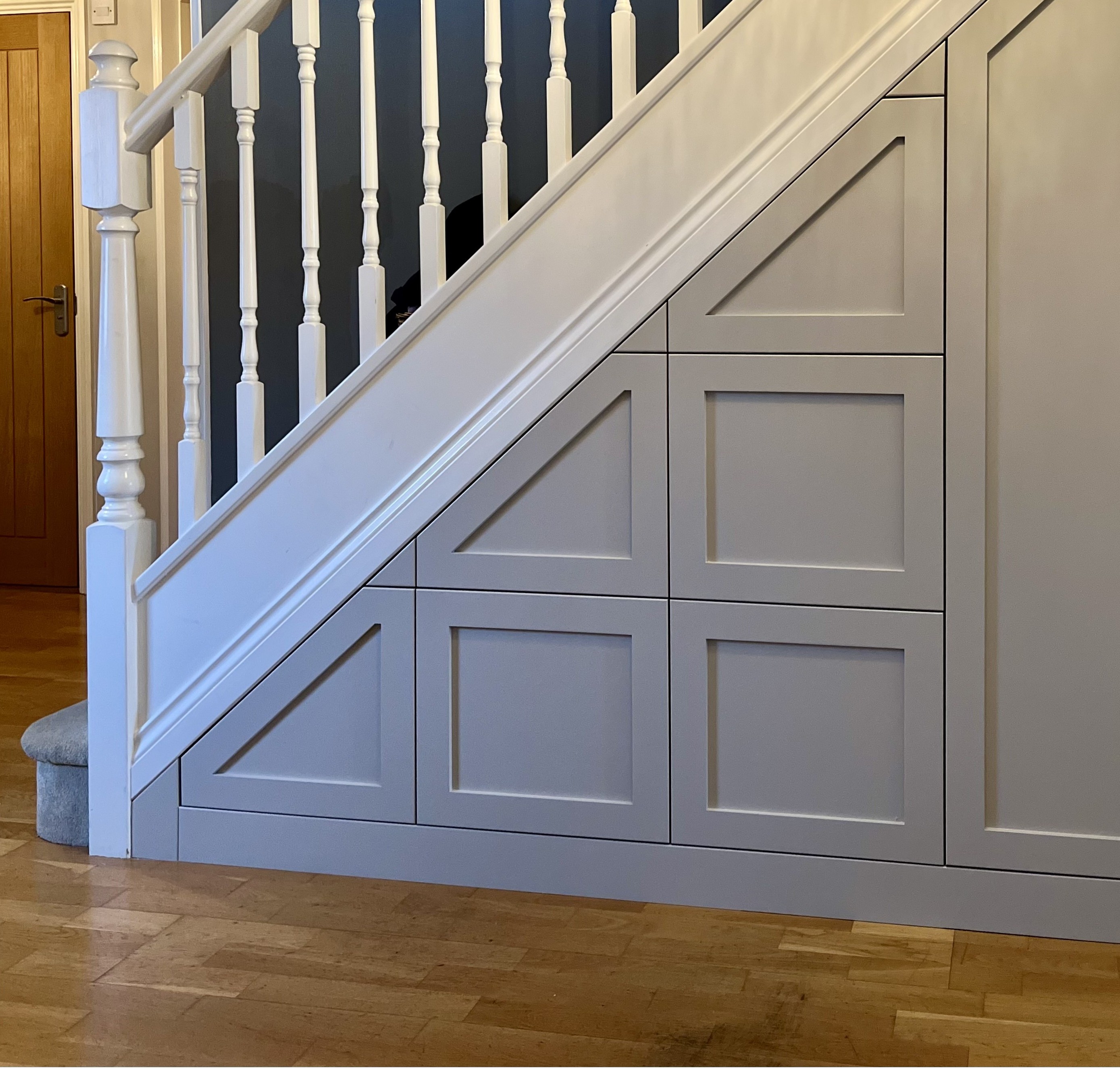 White staircase with decorative spindles and built-in storage cabinets underneath with framed panel design.