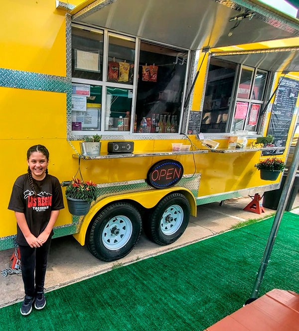 A woman standing in front of a yellow food truck.