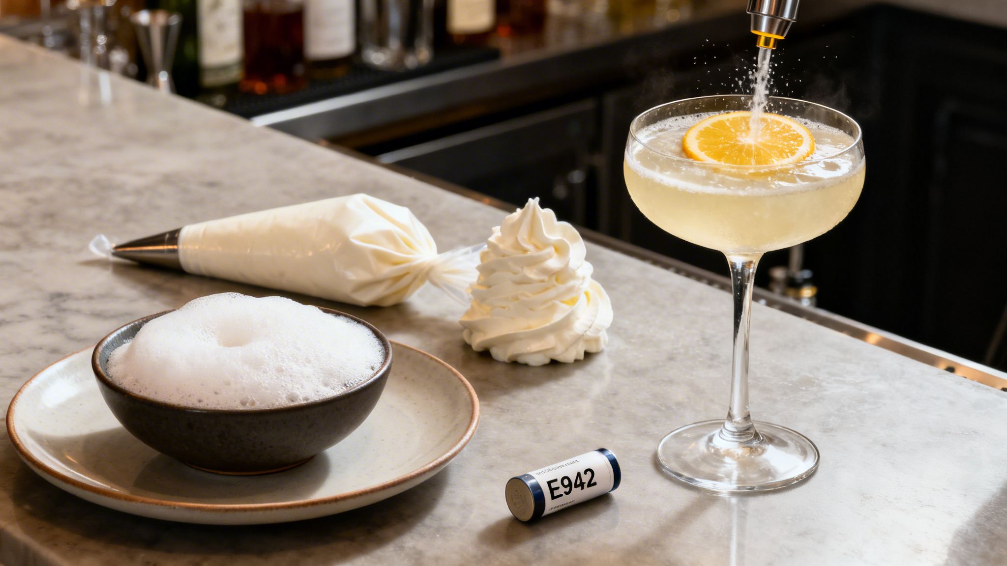 Cocktail with orange slice being topped with gas, alongside whipped cream, foam, and E942 gas cylinder on a bar.