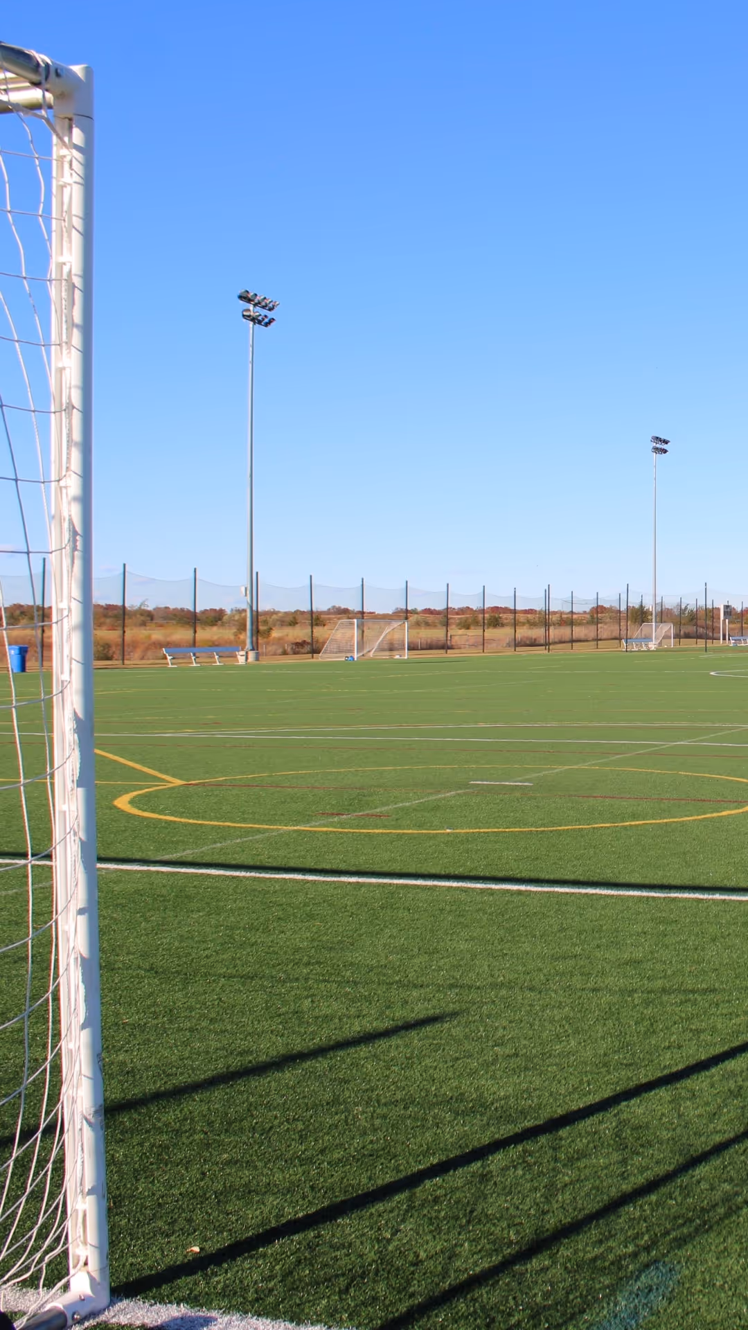 Empty outdoor soccer field with green artificial turf under a clear blue sky.