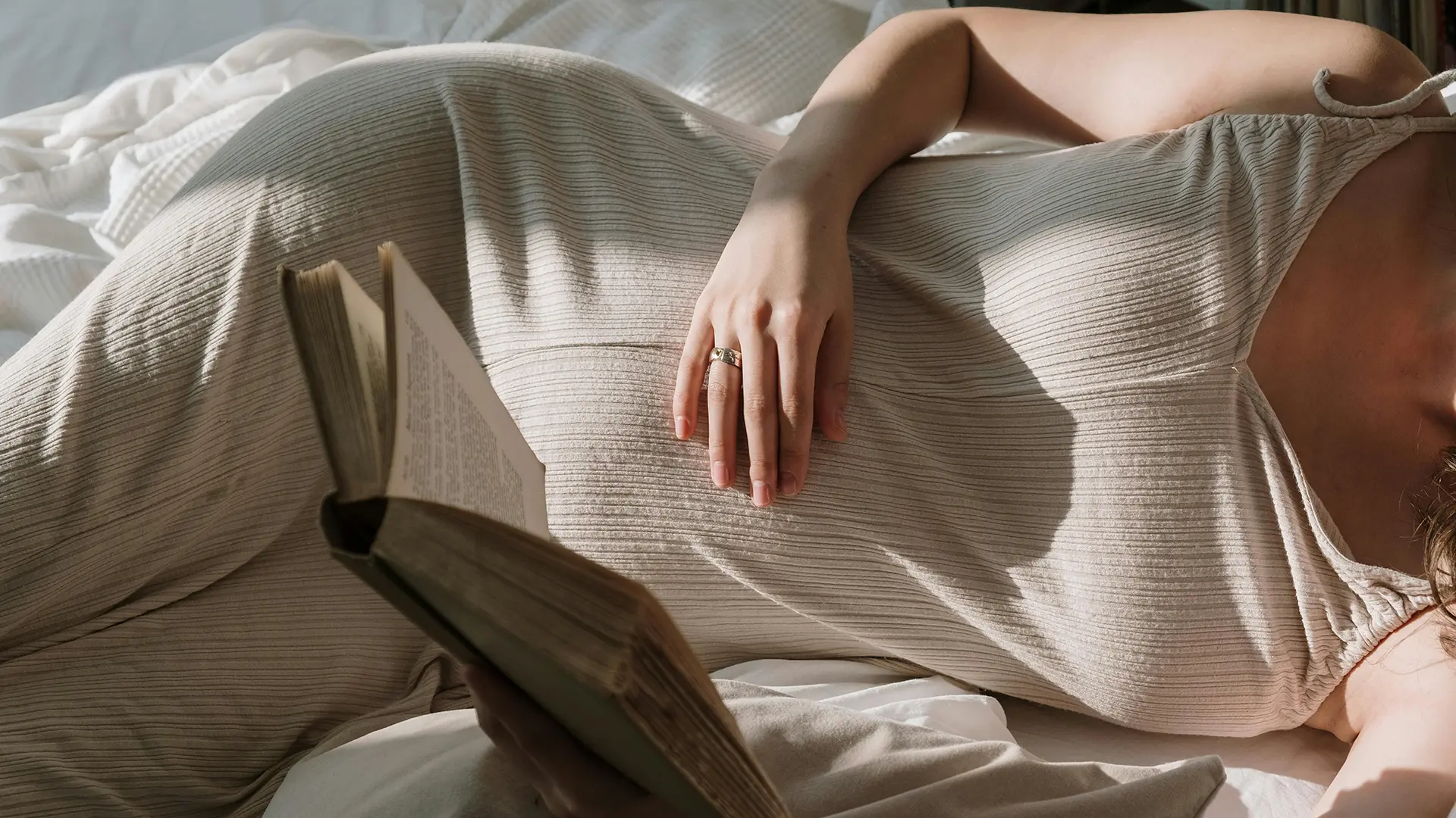 Zwangere vrouw rust met een boek op bed – innesteling herkennen en begrijpen wat er in je lichaam gebeurt.