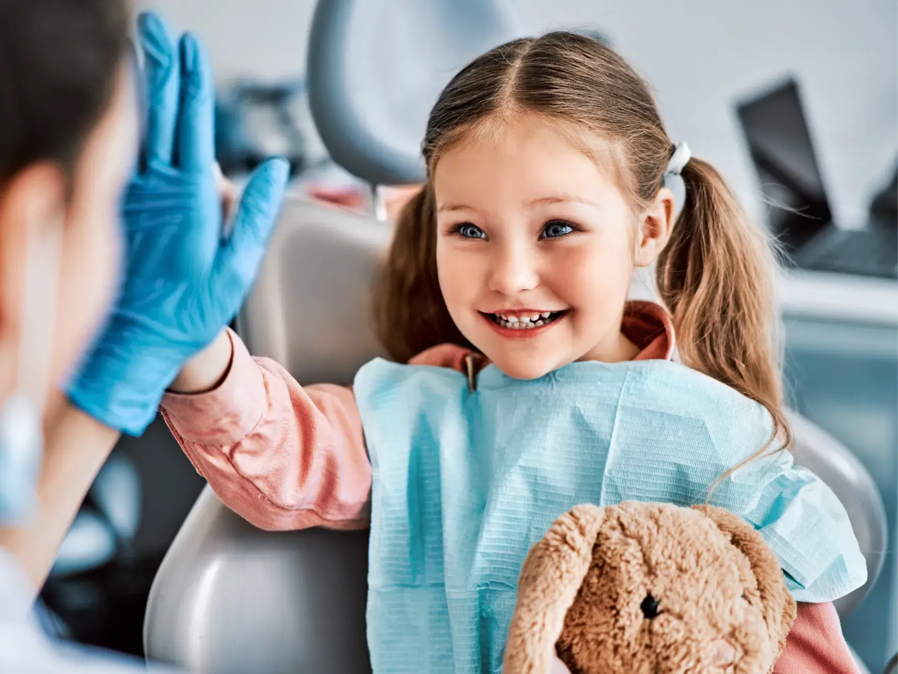 A little girl sitting in a dentist chair with a teddy bear.