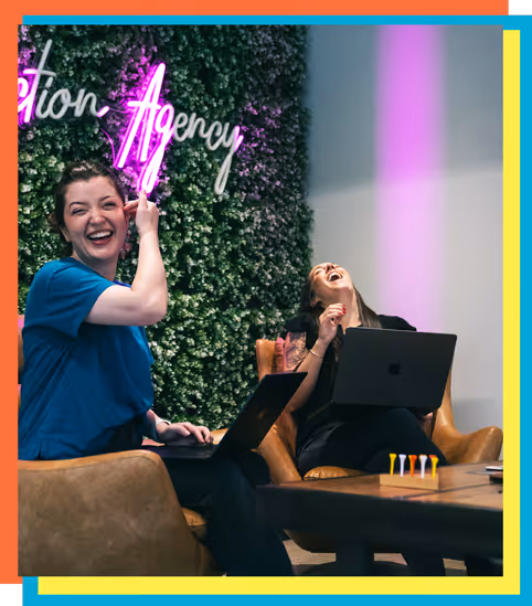 Smiling woman with glasses in an office setting talking to a person holding a cup.