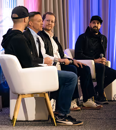 Four men sit on a panel with microphones during a discussion in a conference setting.