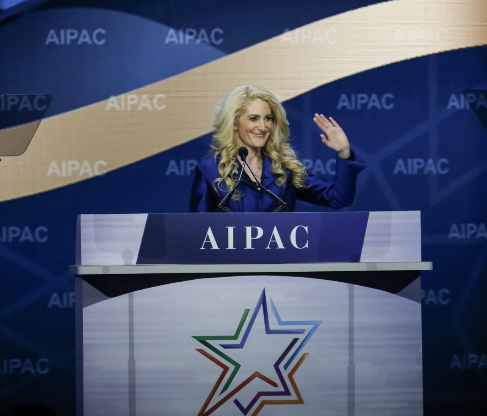 Betsy Berns Korn, past AIPAC President, smiling and waving at a podium on the AIPAC stage