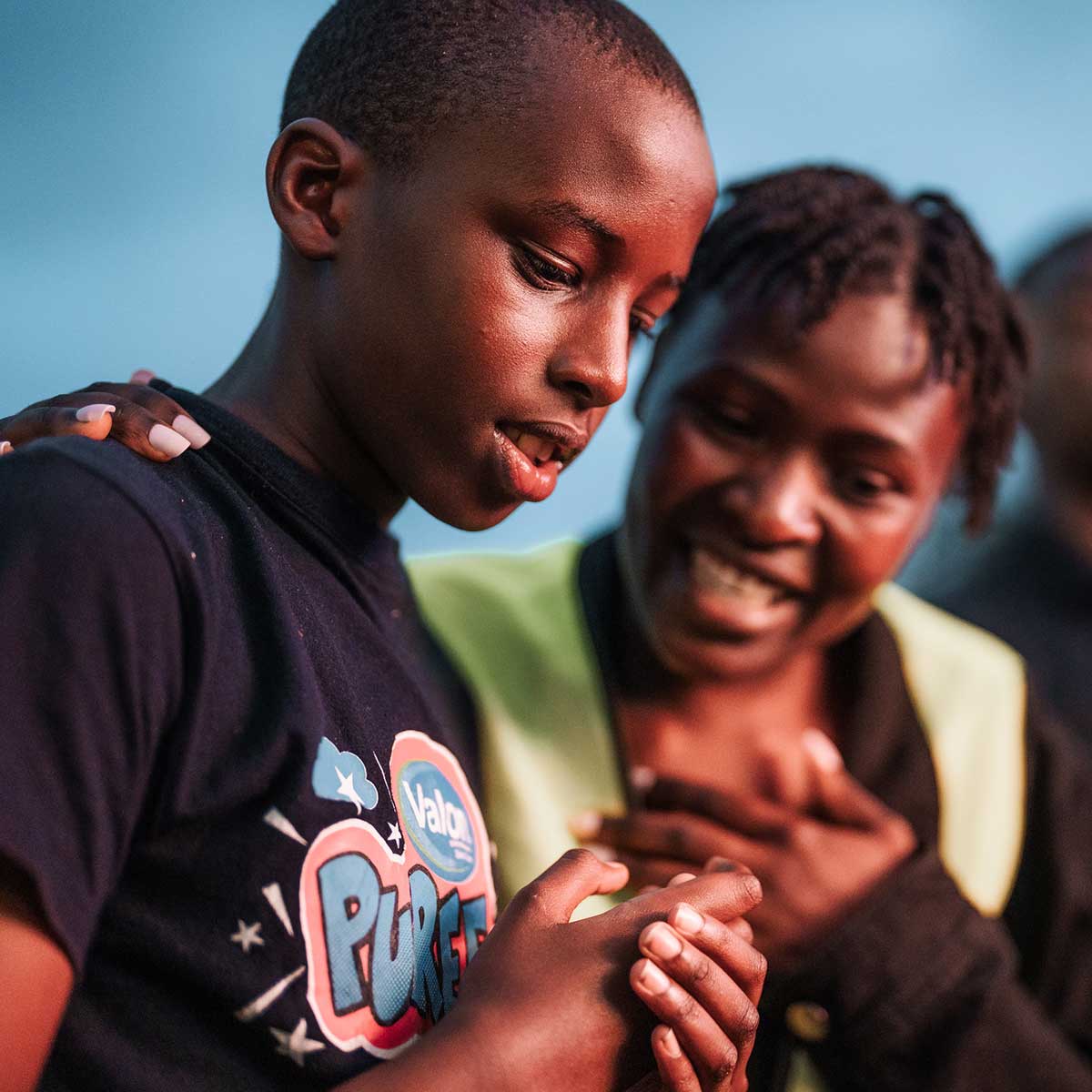 A woman smiling with one hand on her heart and another on the shoulder of a boy