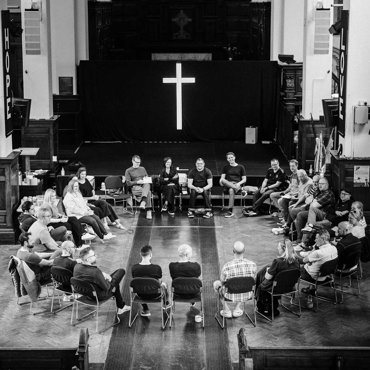 Black and white photo of a group of people sitting in a circle in a church