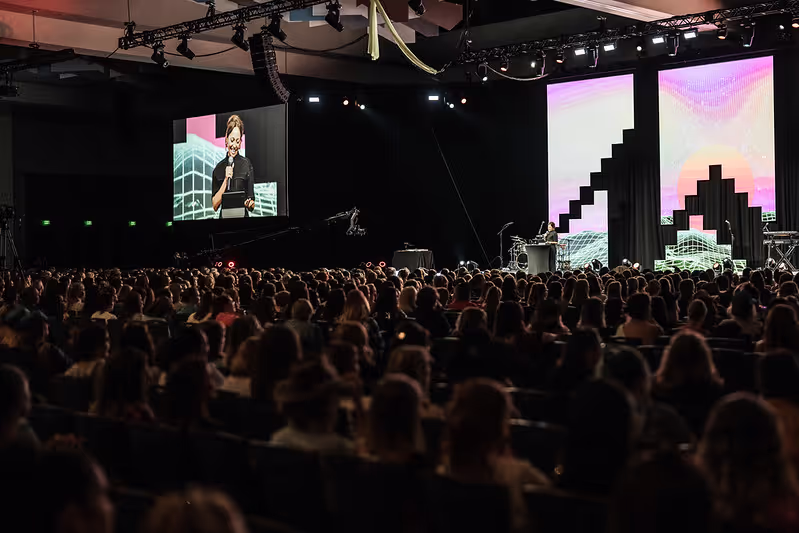A person on stage speaking to a crowd of people