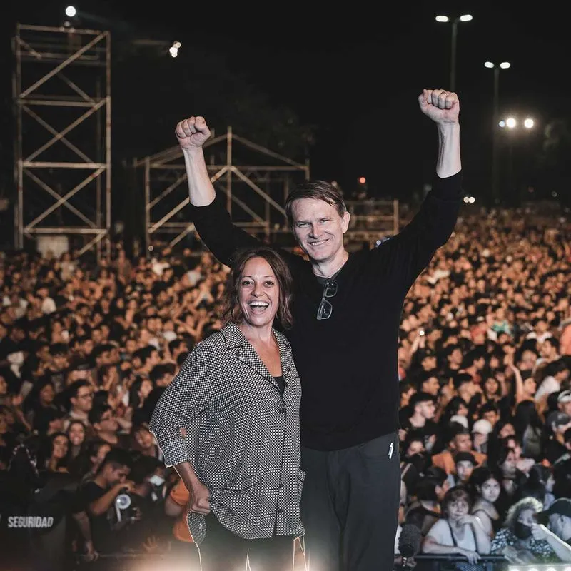 Andrew standing next to Wendy Palau with his arms raised in front of a crowd of people 