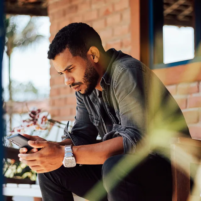 Man sitting outdoors, focused on his smartphone while studying.