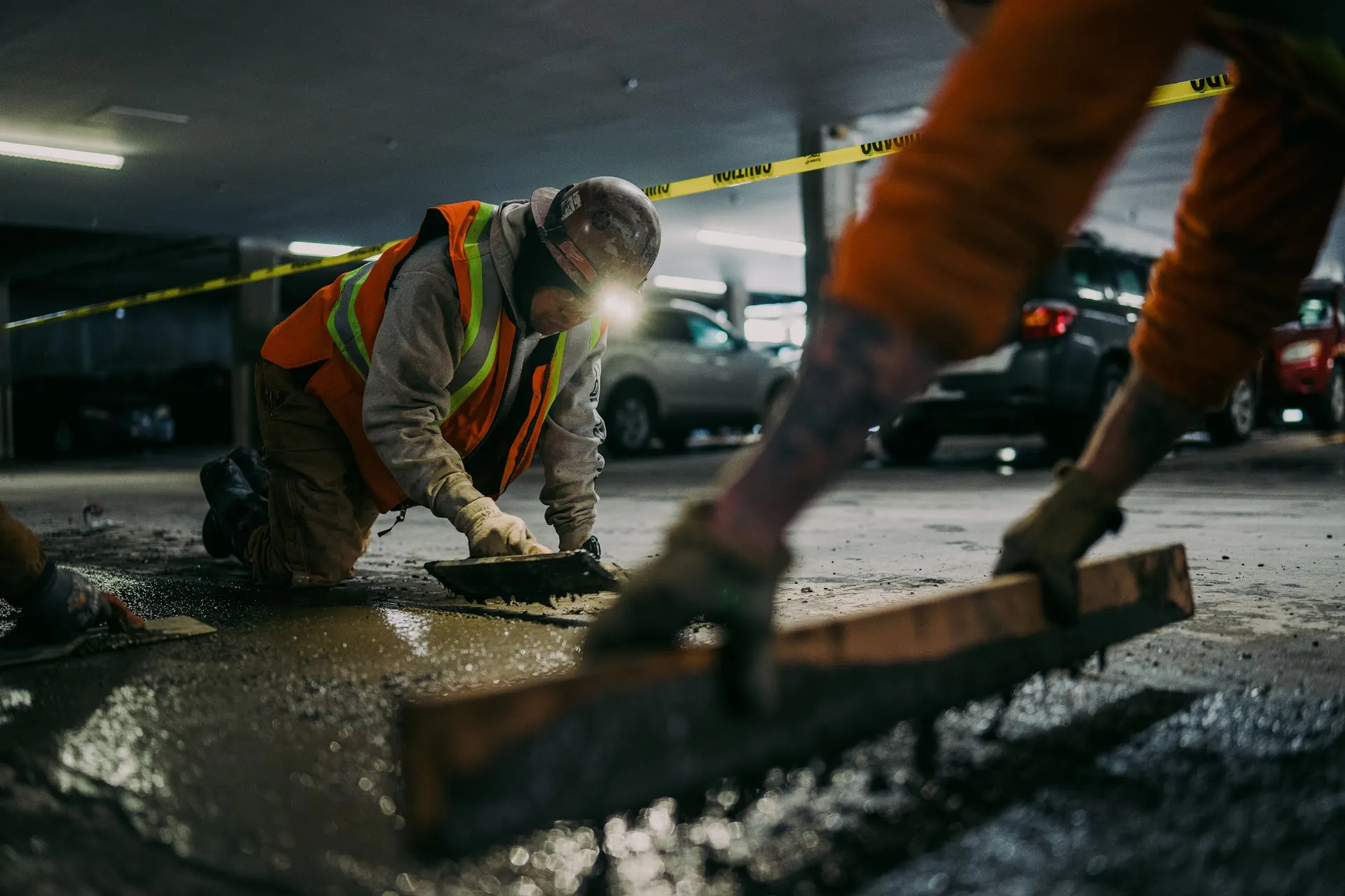 Gerber crew members patch a parking garage deck behind caution tape while cars stay parked nearby.