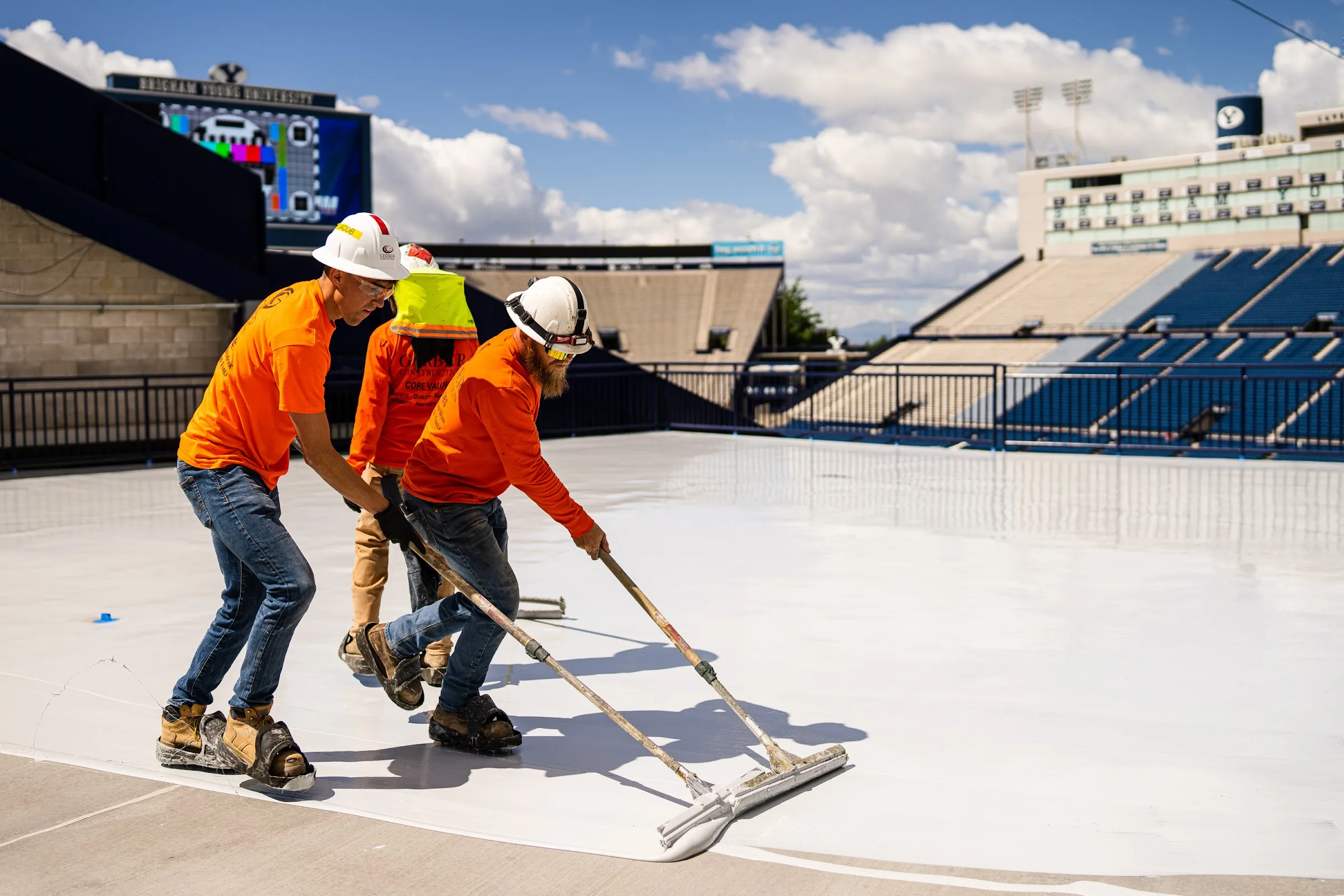 Three Gerber crew members spread a white protective coating across a concourse deck with squeegees.