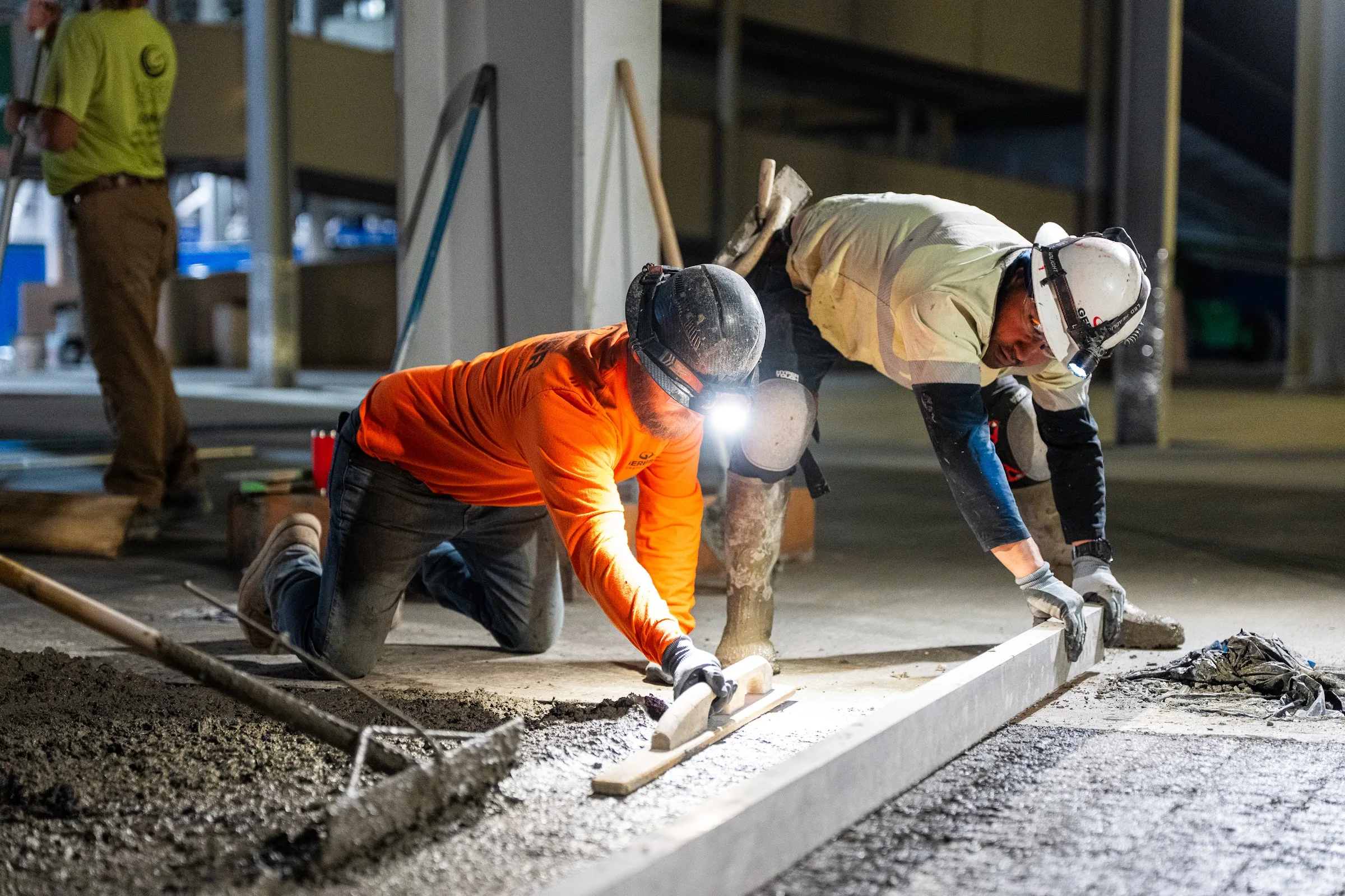 Gerber crew members finish fresh concrete at night with hand tools.