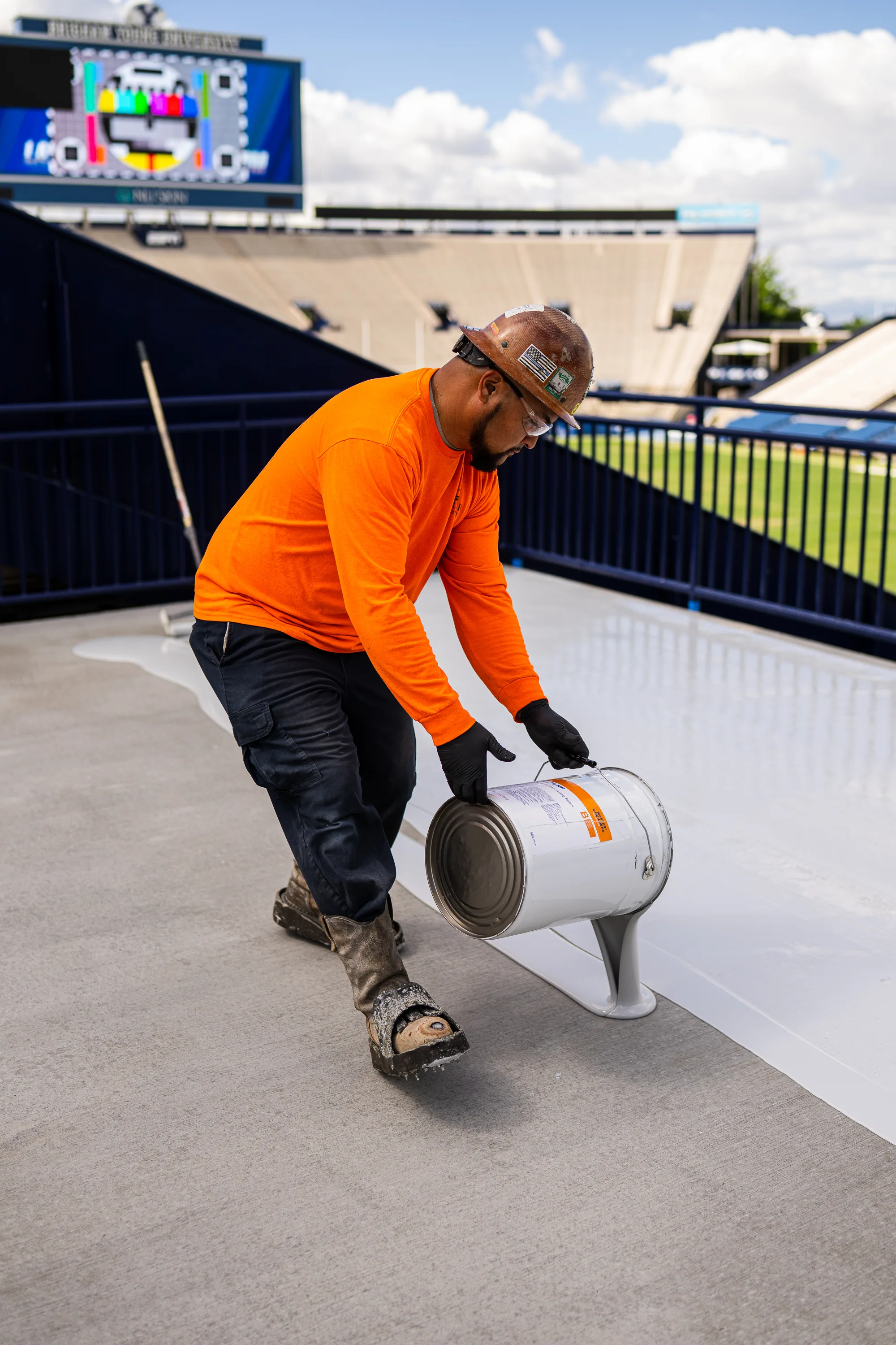 A crew member pours protective coating onto a prepared concrete deck.