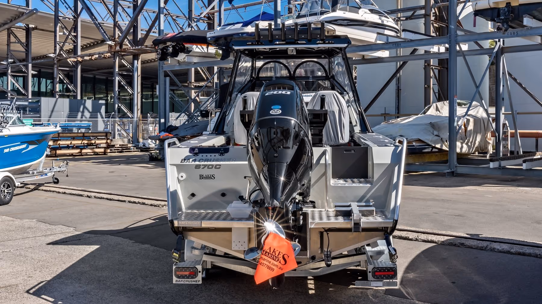 A boat in a dockyard featuring a powerful motor and reflective surface. Boats and covered vehicles in the background convey an industrial setting.