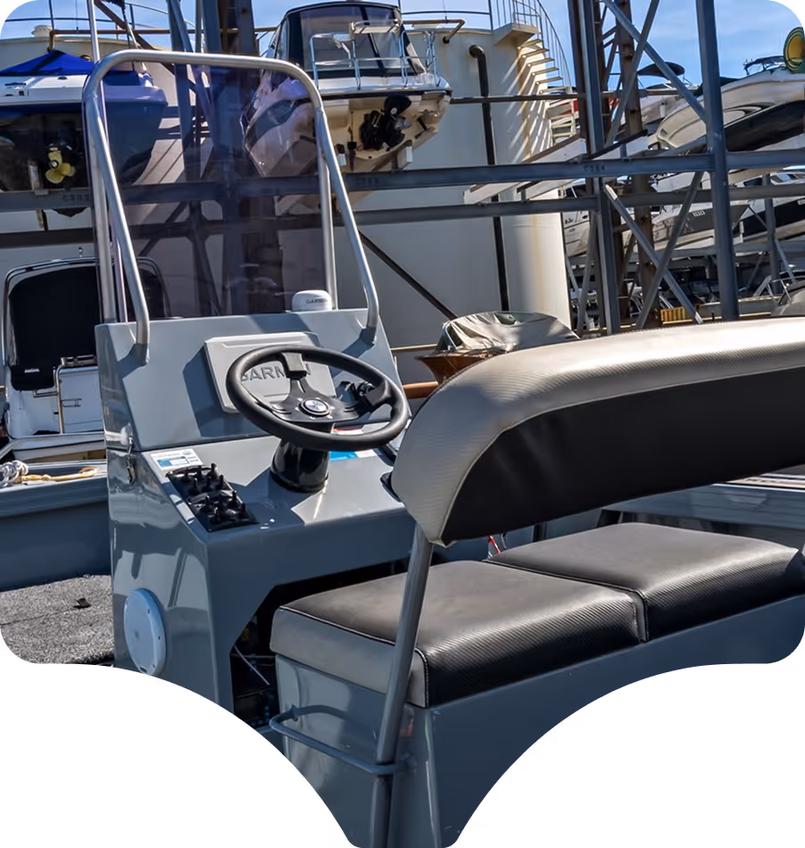 Steering console of a motorboat with a black and gray seat, navigation equipment, and a clear windshield. Docked with other boats in the background.