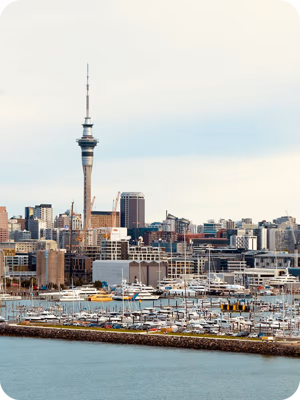 View of Auckland city skyline with Sky Tower and boats docked in the harbor.