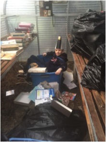 Nate, sitting in a plastic tub with a cone on his head in a room full of debris.