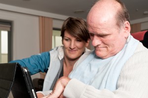 man in wheelchair using an ipad, assisted by a woman