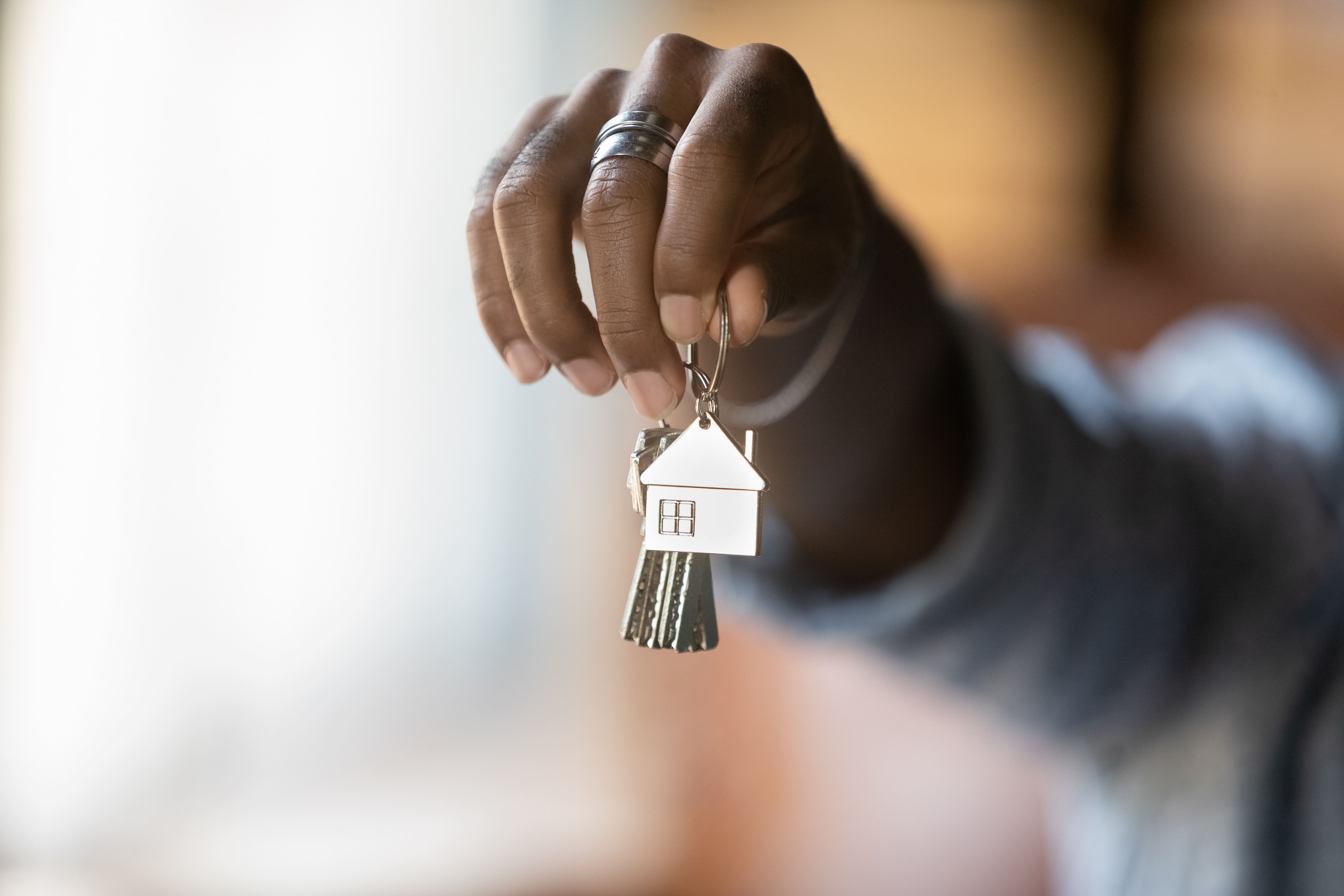 Outstretched hand holding a set of keys with a silver house charm on the keyring