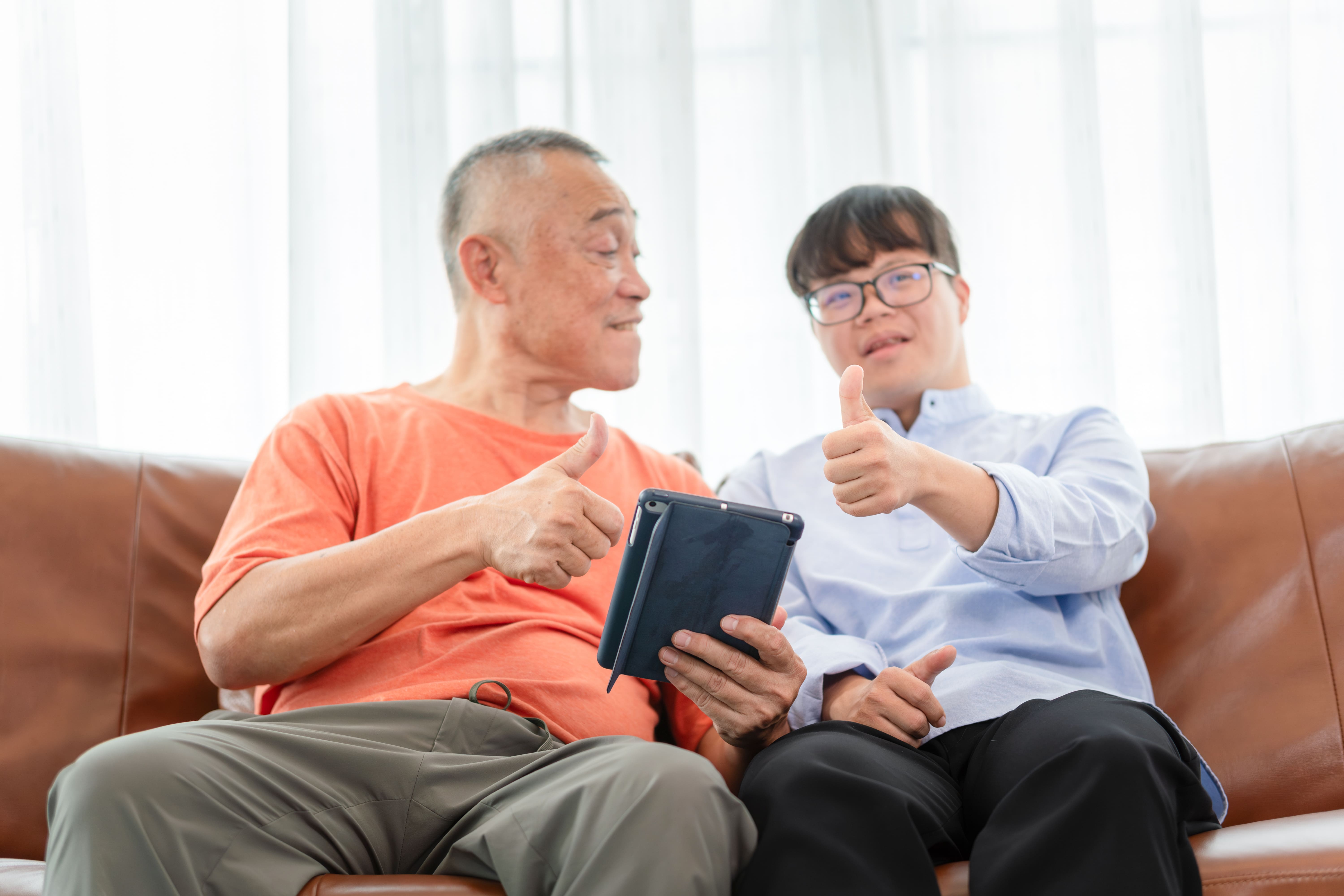 Father and son sit on couch with iPad giving thumbs up