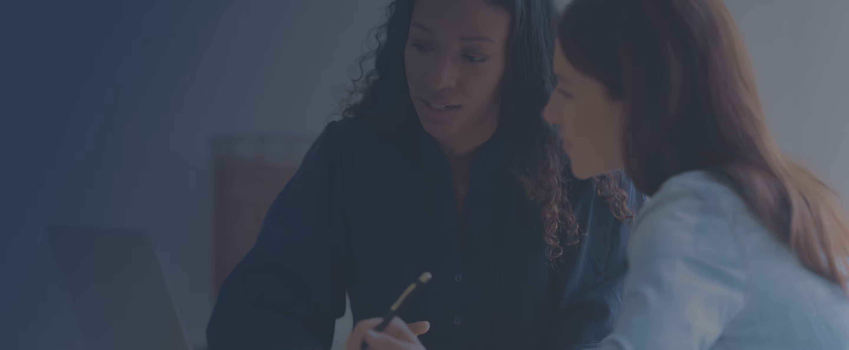 Two women sitting closely and collaborating while looking at a laptop screen.