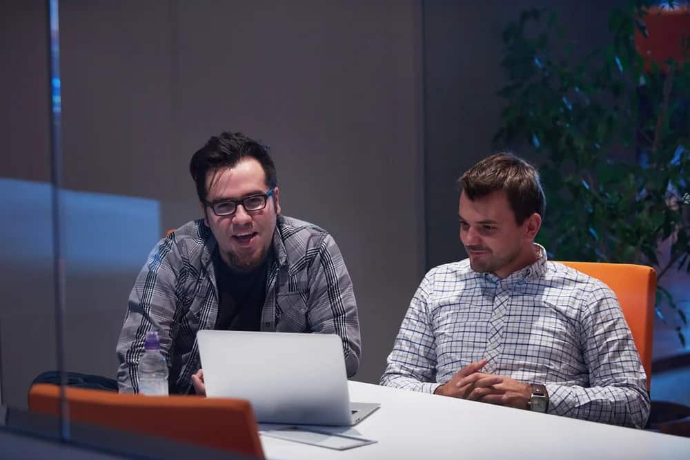Two men sitting at a table looking at a laptop during a meeting in an office.