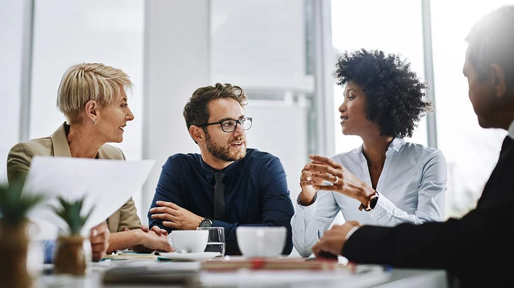 Four diverse businesspeople sitting at a table having an engaged discussion in a bright office.
