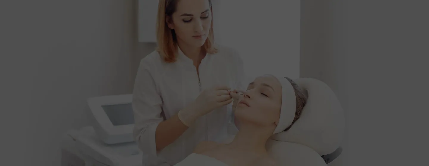 A cosmetologist in gloves applies a treatment on a woman's nose in a skincare clinic.